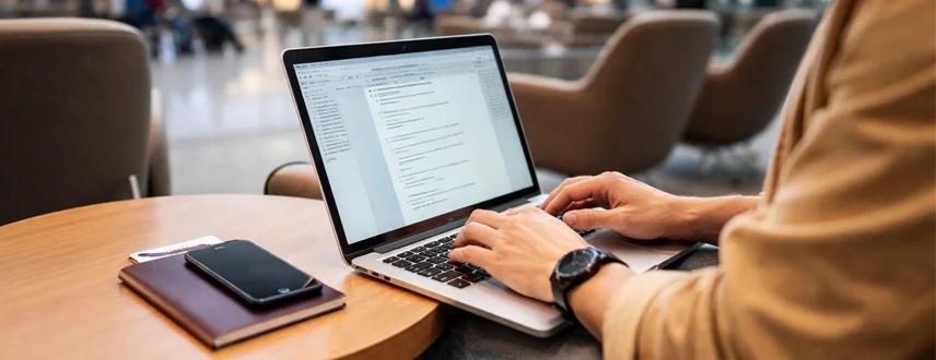 Traveller using a laptop and phone at an airport before a trip